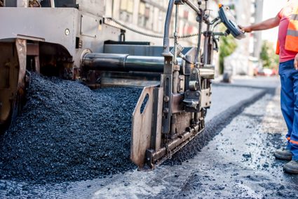 Asphalt pavement being installed showing loose aggregates in the foreground and slightly compressed asphalt in the background