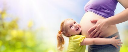 Kobieta w ciąży blisko terminu porodu przytulająca małą dziewczynkę o jasnych włosach.