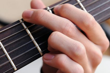 An image of a guitar fingerboard with a hand fretting the strings