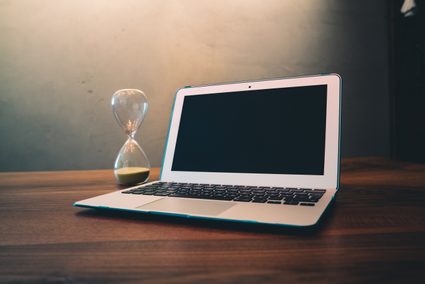 An hourglass and an open laptop lying on a table.