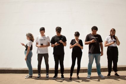 A group of six teenagers holding and staring at their cell phones.