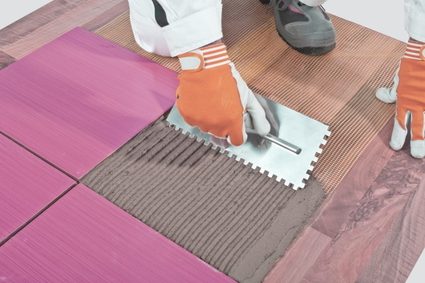 Image of a tile installer applying thinset onto the floor using a notched trowel that leaves a uniform thickness thinset beads on the floor.